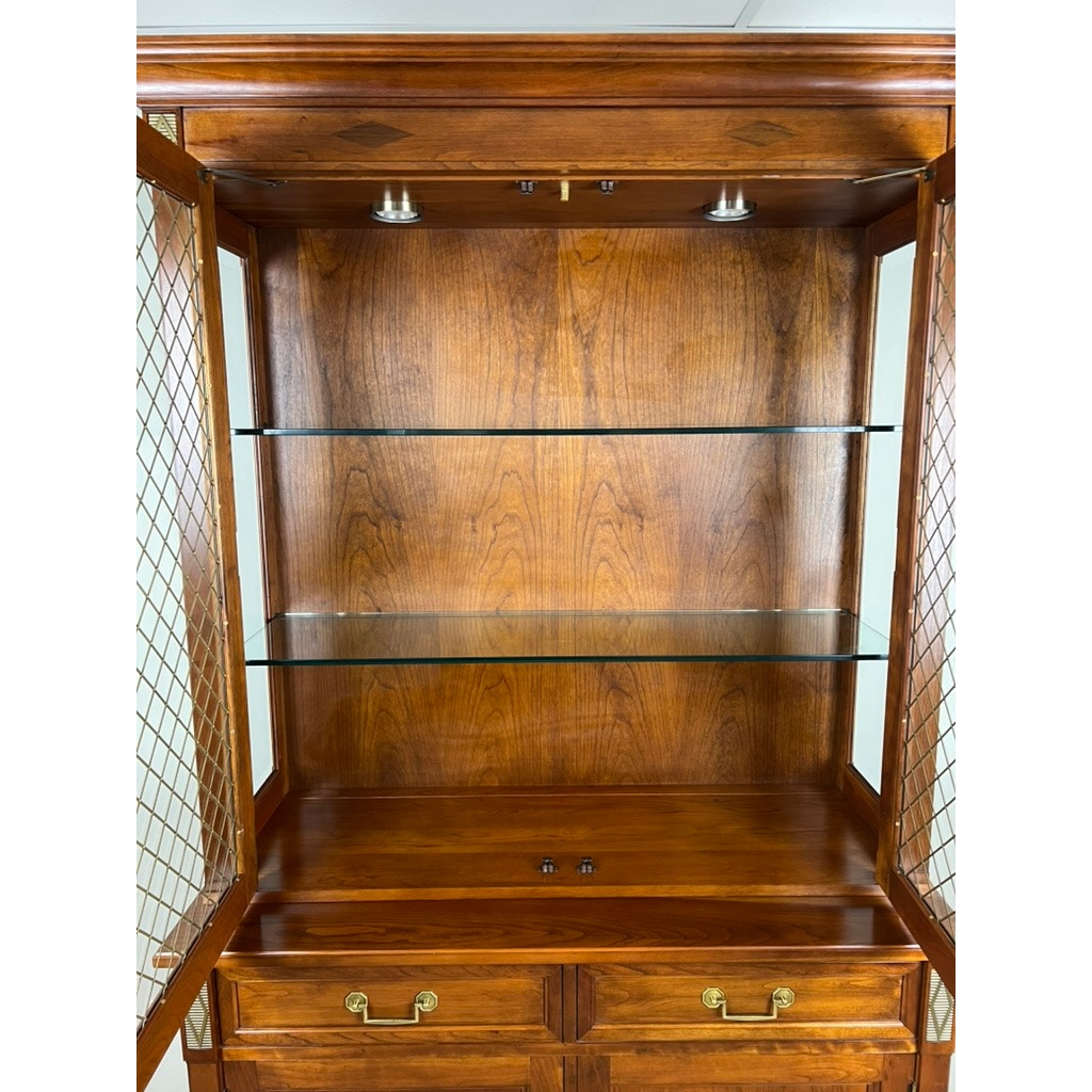 The Stickley Vintage William IV Style Cherry Glass Door Bookcase features glass shelves, a cherry finish, glass doors, brass handles, metal lattice side panels, and interior top lighting.