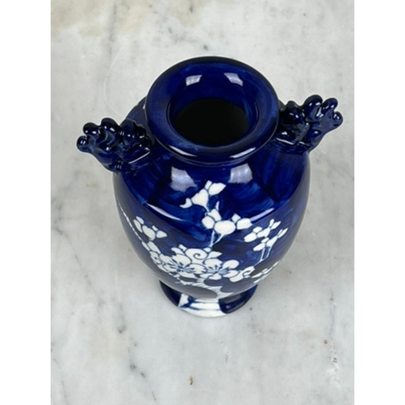 The Vintage Japanese Blue and White Floral Bud Vase features white floral patterns and two decorative handles, photographed from above on a light marble surface. Brand is unknown.