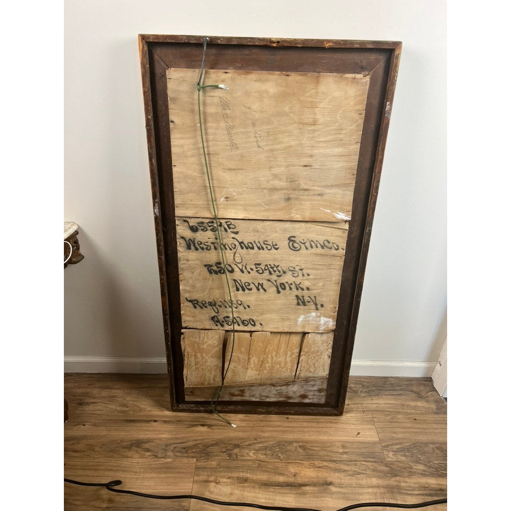 An Antique American Empire Parcel Gilt Flame Mahogany Ogee Wall Mirror (mid-19th century) rests face down on a wooden floor, showing wood backing with handwritten “Westinghouse Erica, 560 Oak Street, New York, Repasso, NY” and an attached hanging wire.