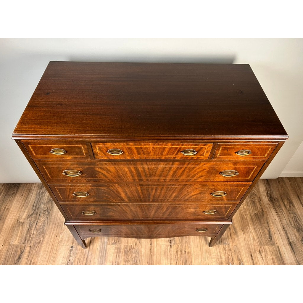 A Vintage Dutch Woodcraft Shops Federal Style Flame Mahogany Chest on Stand (c. 1945–1955) with five drawers, brass handles, and a polished finish sits on a wood floor against a white wall, viewed from above—a fine example of the craftsmanship from Dutch Woodcraft Shops.