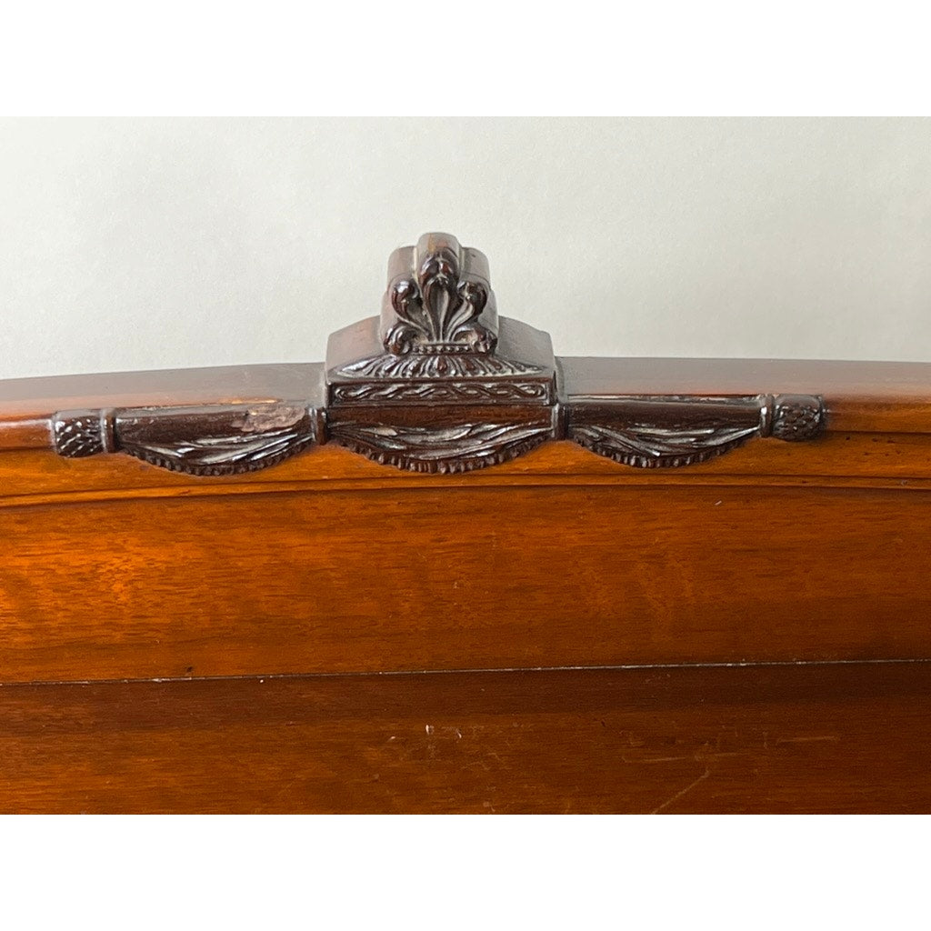 Close-up of ornate dark wood carving on an Antique Depression Era Mahogany Two Over Three Chest of Drawers c. 1930s, featuring a central floral motif and draped garland design, set against a light background. Brand unknown.