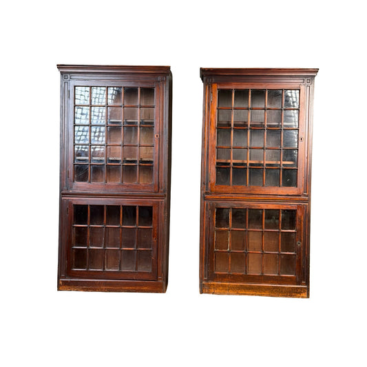 A pair of mid-19th century New England cherry glazed display cupboards, dating from circa 1840–1860, each featuring upper and lower sections with glass-paned doors, stand side by side on a white background.