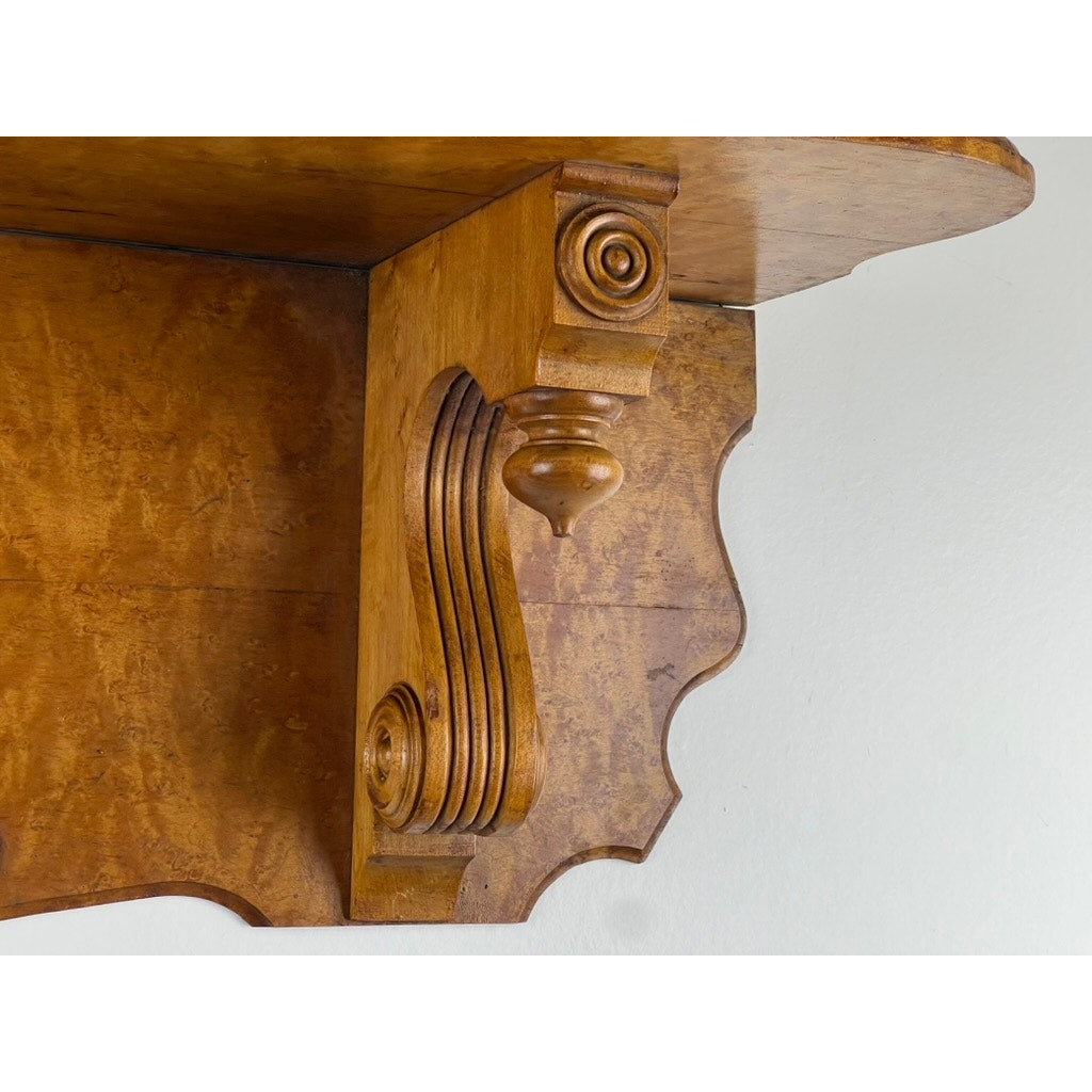 Close-up of an Antique Victorian Birdseye Maple Wall Shelf (late 19th century) with ornate scrollwork and carved details, mounted on a light-colored wall. Brand: Unknown.