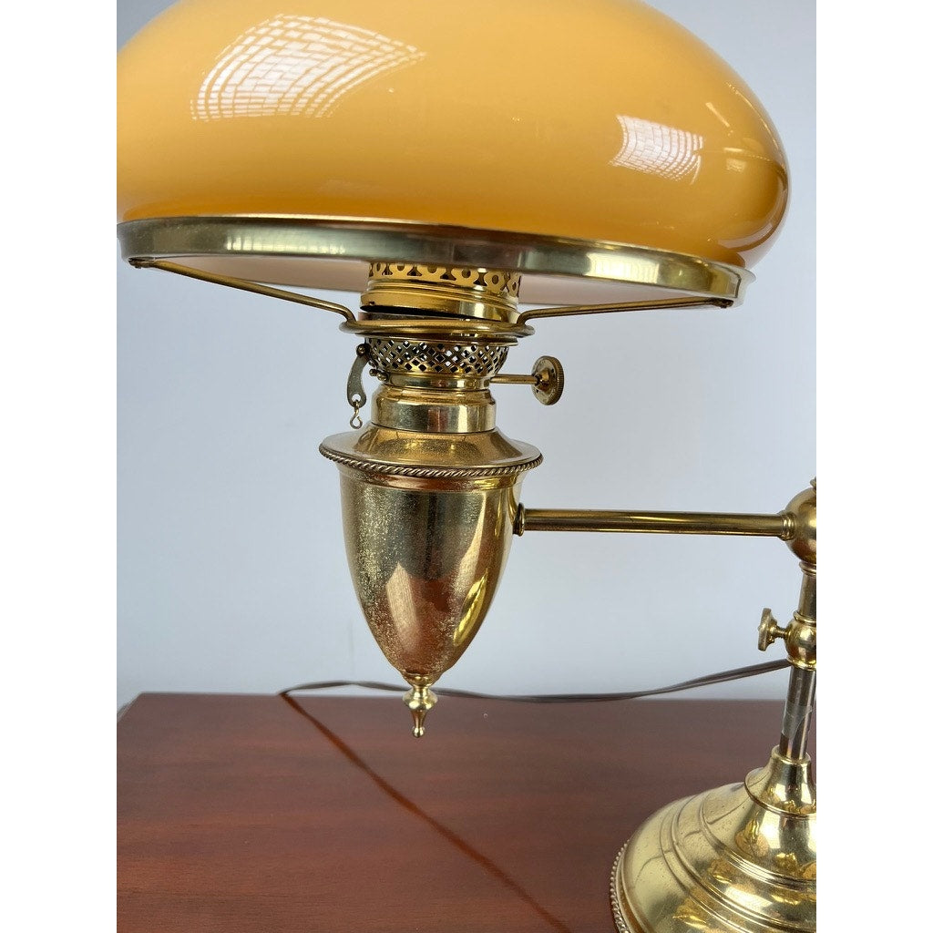 A close-up of an Antique Bradley and Hubbard Brass Double-arm Student Lamp with caramel shades showcases the brand’s ornate metalwork and reflective finish as it sits on a wooden surface.