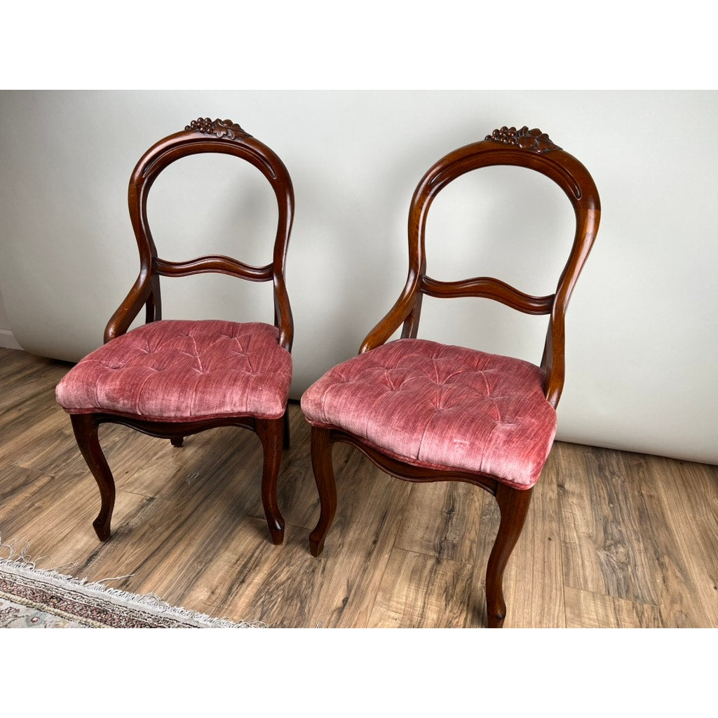 An Antique Pair Victorian Walnut Balloon Back Tufted Side Chairs (late 19th century) with red velvet seats are positioned side by side on a wooden floor against a plain light-colored wall.