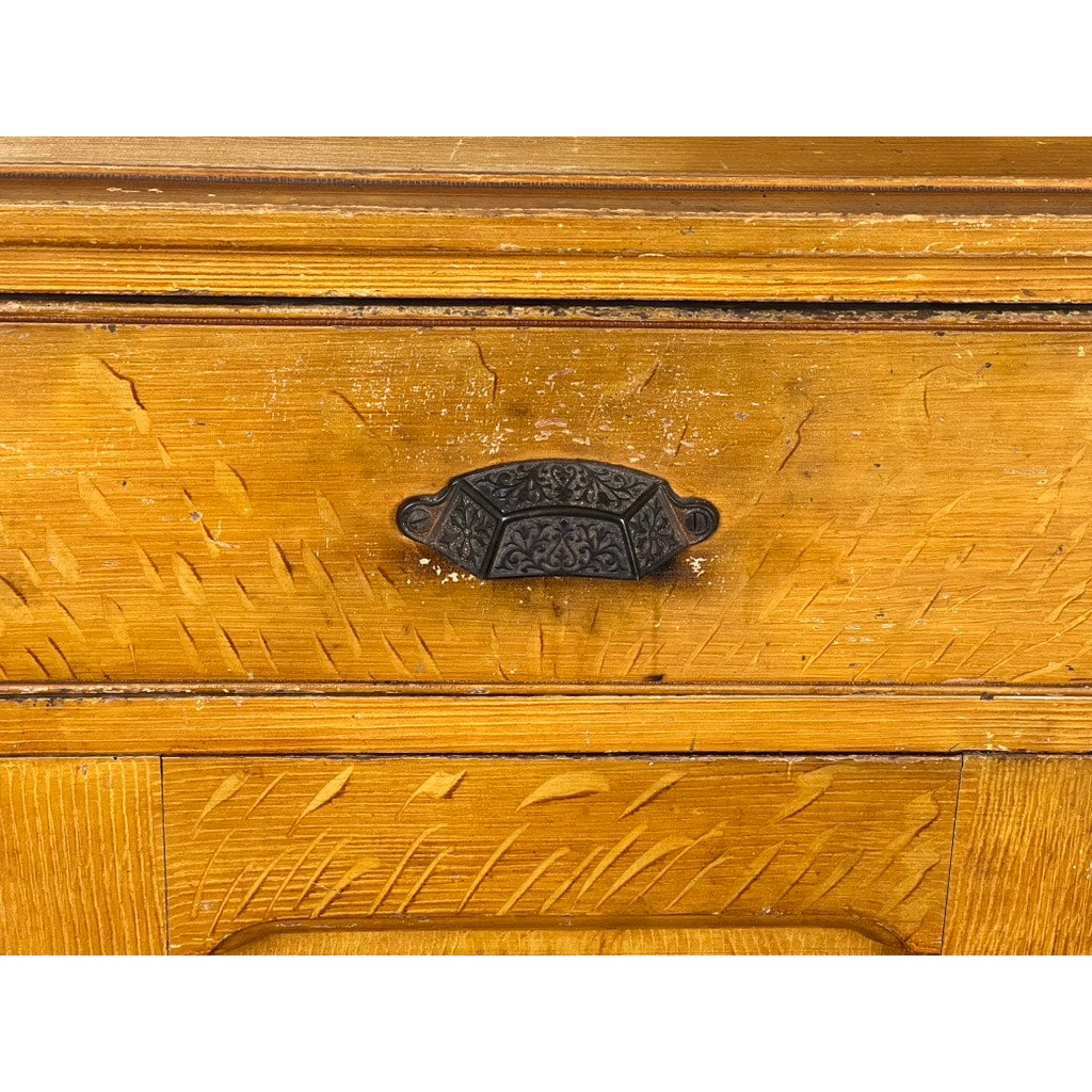 Close-up of a wooden drawer from an Antique Victorian Grain Painted Country Jelly Cupboard c. 1870, showing visible grain, scratches, and a decorative dark metal pull handle at the center. Brand: None/Unknown.