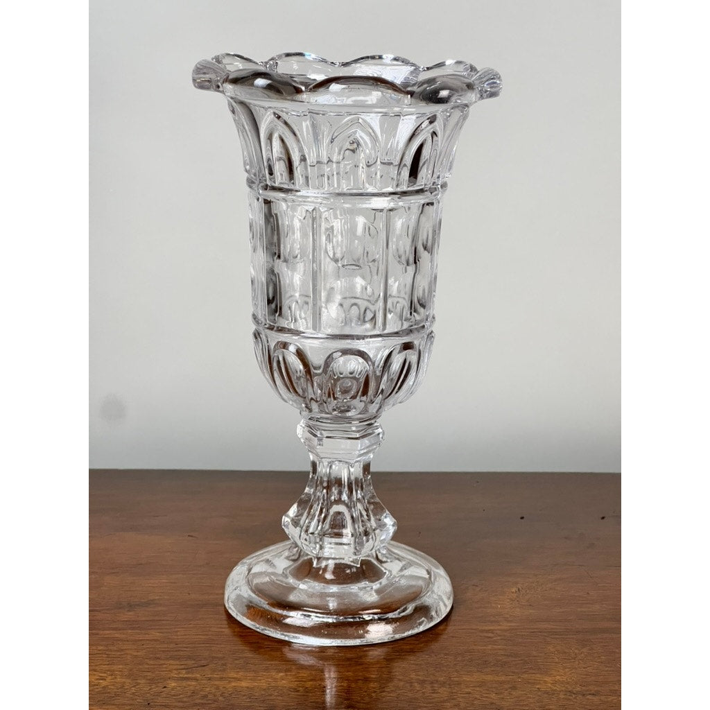 An Antique Boston & Sandwich Glass Co. Gothic Arch pressed glass celery vase (c. 1860–1880) by Sandwich Glass features an ornate, fluted scalloped rim and round pedestal base displayed on a wooden surface.
