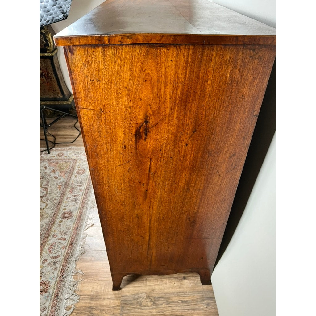 A close-up of the side of an Antique George III Two Over Four Chest with French feet (early 19th century) shows its rich grain and warm brown finish, standing on hardwood near a patterned rug and white wall—a classic Georgian piece.