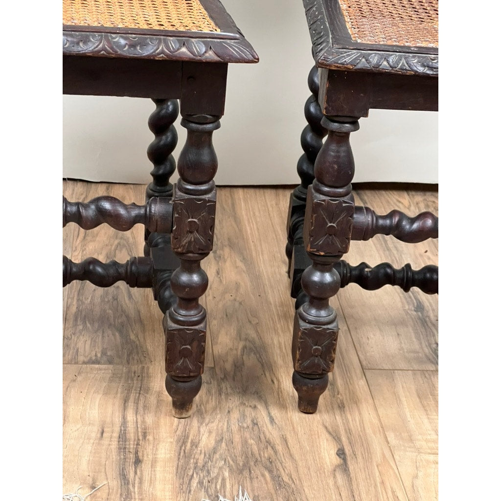 A pair of antique French walnut hunting chairs (late 19th c.) features intricately carved legs and cane seats, displayed side by side on a light wood floor against a plain white wall. The close-up highlights the ornate front legs and crossbars.