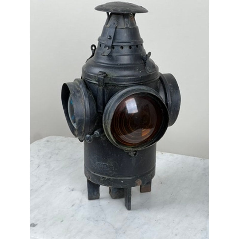 An Antique Illinois Central Railroad Signal Lantern by Dressel Arlington NJ stands upright on a white marble surface with a round main lens and side lenses, set against a plain light background.
