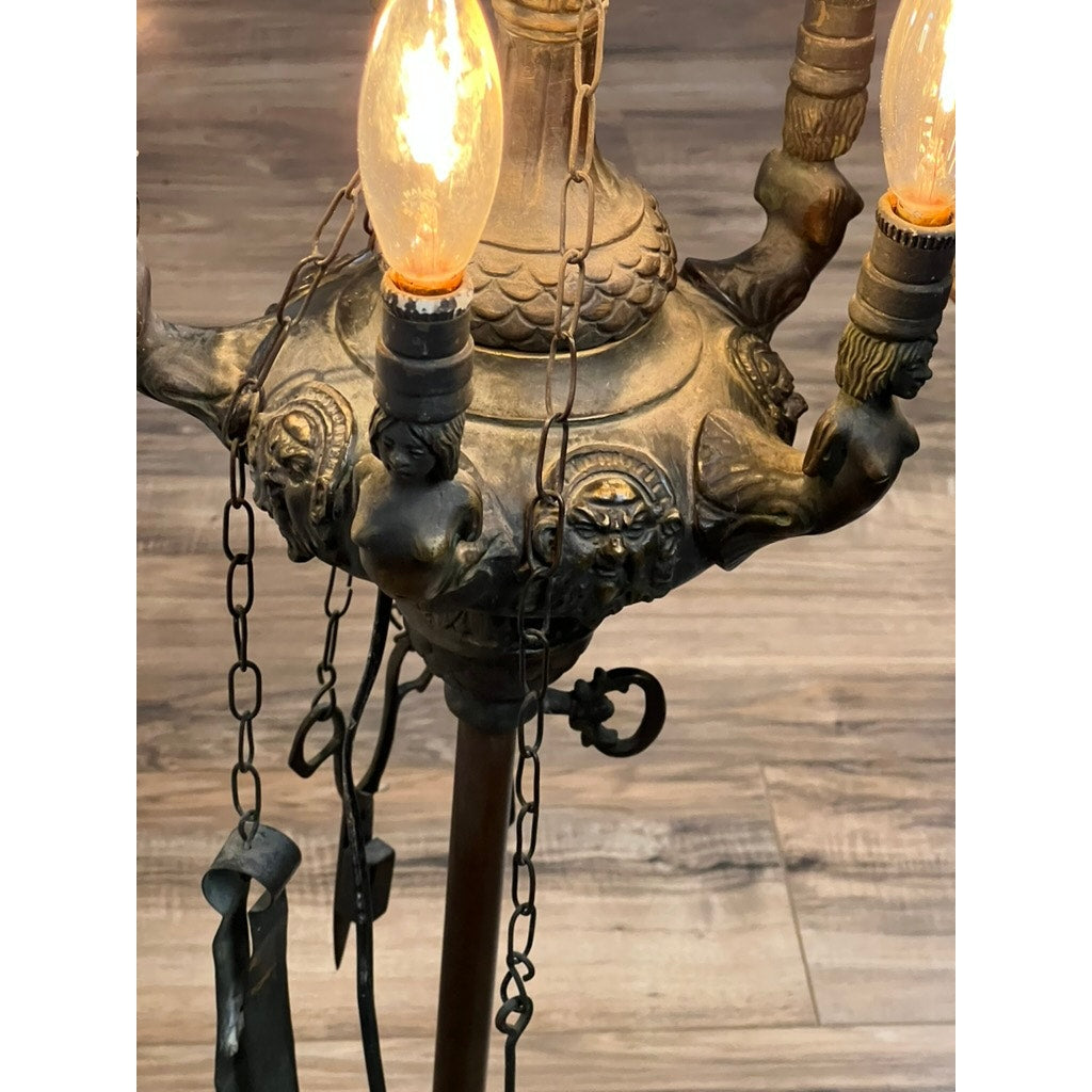 The Antique Five Burner Lucerne Whale Oil Lamp features vintage-style bulbs, sculpted lion heads, and decorative chains, set on a wooden floor beside its Napoleon I Fireplace Screen Shade. Brand is unknown.