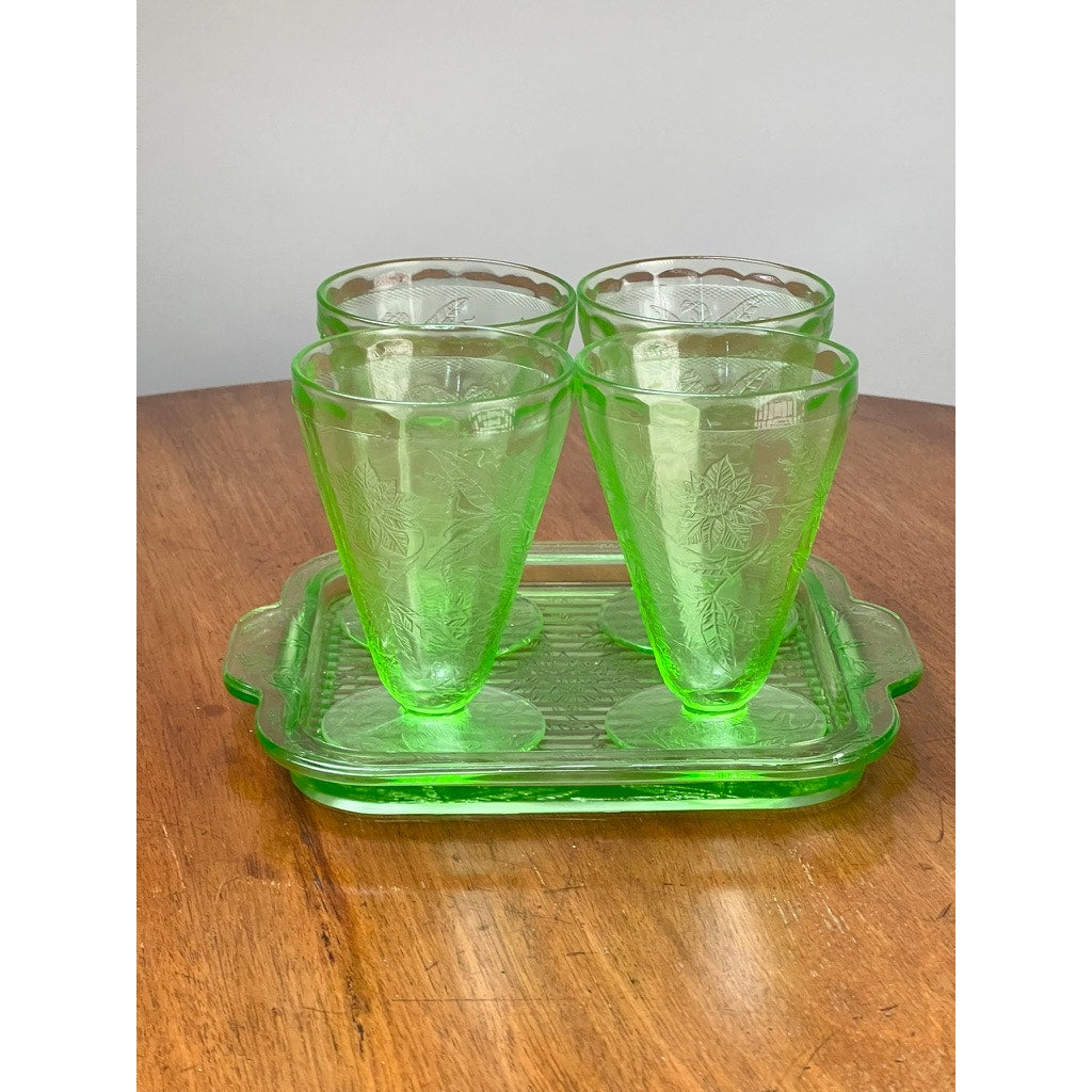 The Antique Jeannette Glass Co. Green Uranium Floral Poinsettia 5-Piece Beverage Set (c. 1930s) features four tumblers with floral design on a matching handled tray, displayed on wood against a light background.