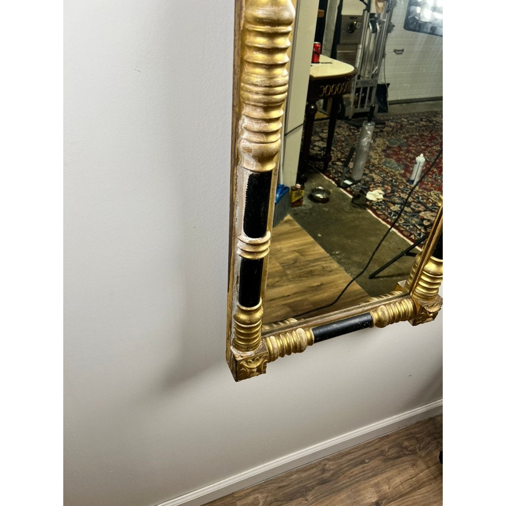 A close-up of an Antique Federal Period Giltwood Mirror with Rosette Corners and Cornucopia c. 1830 hangs on a white wall, reflecting a patterned rug, wooden floor, and studio equipment in the background.