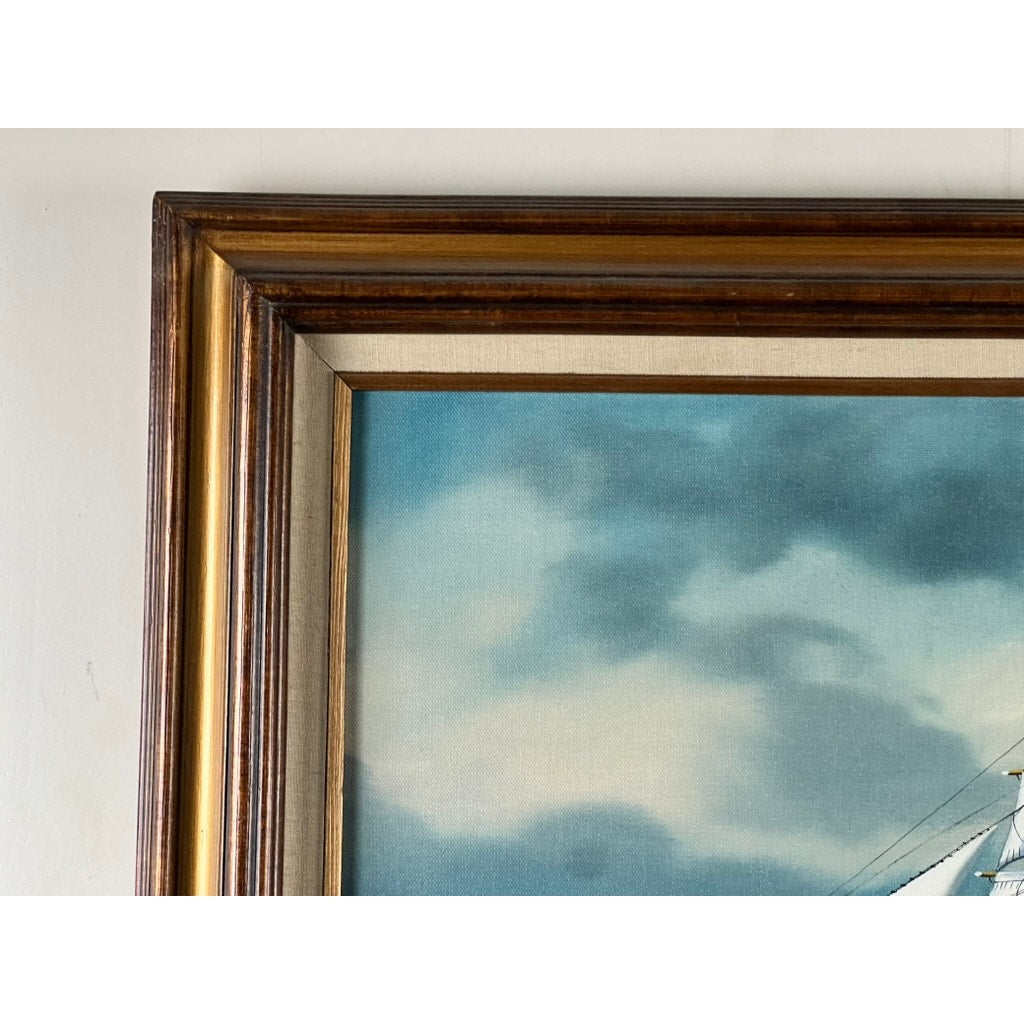 Close-up of the top left corner of “Tall Ship Under Sail” oil on canvas by John Richard Perry ME 1984, showing a golden-brown wooden frame and part of the artwork’s blue sky with white clouds.