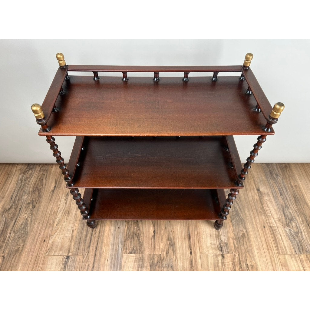 A Vintage Bobbin-turned, Three Shelf Wooden étagère or Whatnot with turned legs and brass finials stands on a wooden floor against a light-colored wall. Brand: None and/or Unknown.