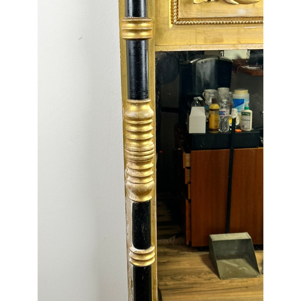 A close-up of an Antique Federal Period Giltwood Mirror with Rosette Corners and Cornucopia c. 1830 reflects shelves filled with bottles and a brown cabinet in the background.
