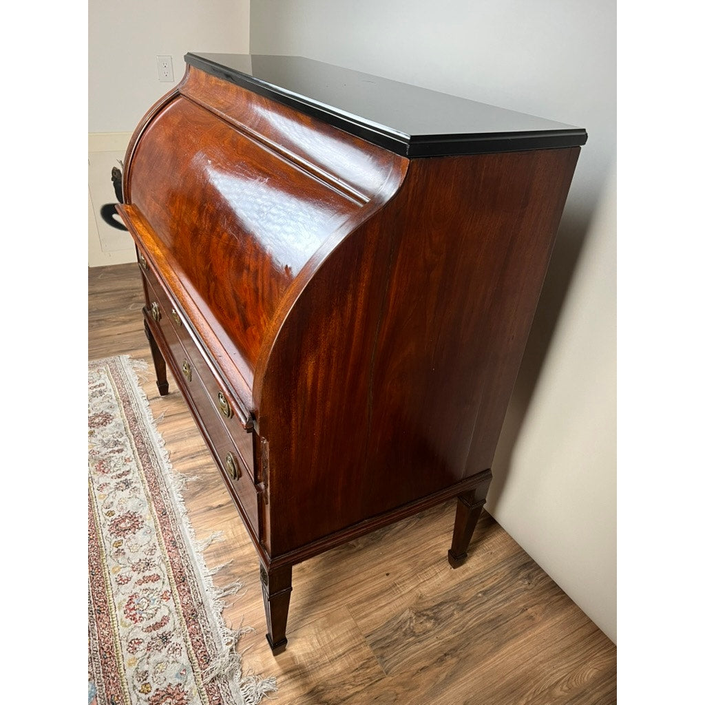 An Antique Directoire Style French Cylinder Desk with a slate top from the late 19th century stands on a wooden floor beside a patterned rug and a light-colored wall.