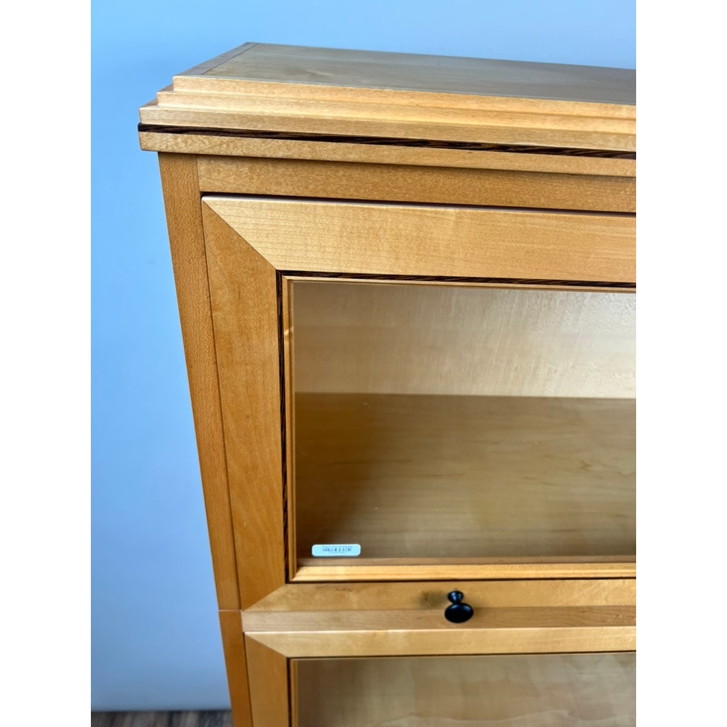 Close-up of the upper section of a Vintage Bench Made Maple with Wenge Inlay Three Stack Barrister Bookcase, featuring glass doors, a black knob, and an interior label. The light wood cabinet stands against a plain, light-colored wall.