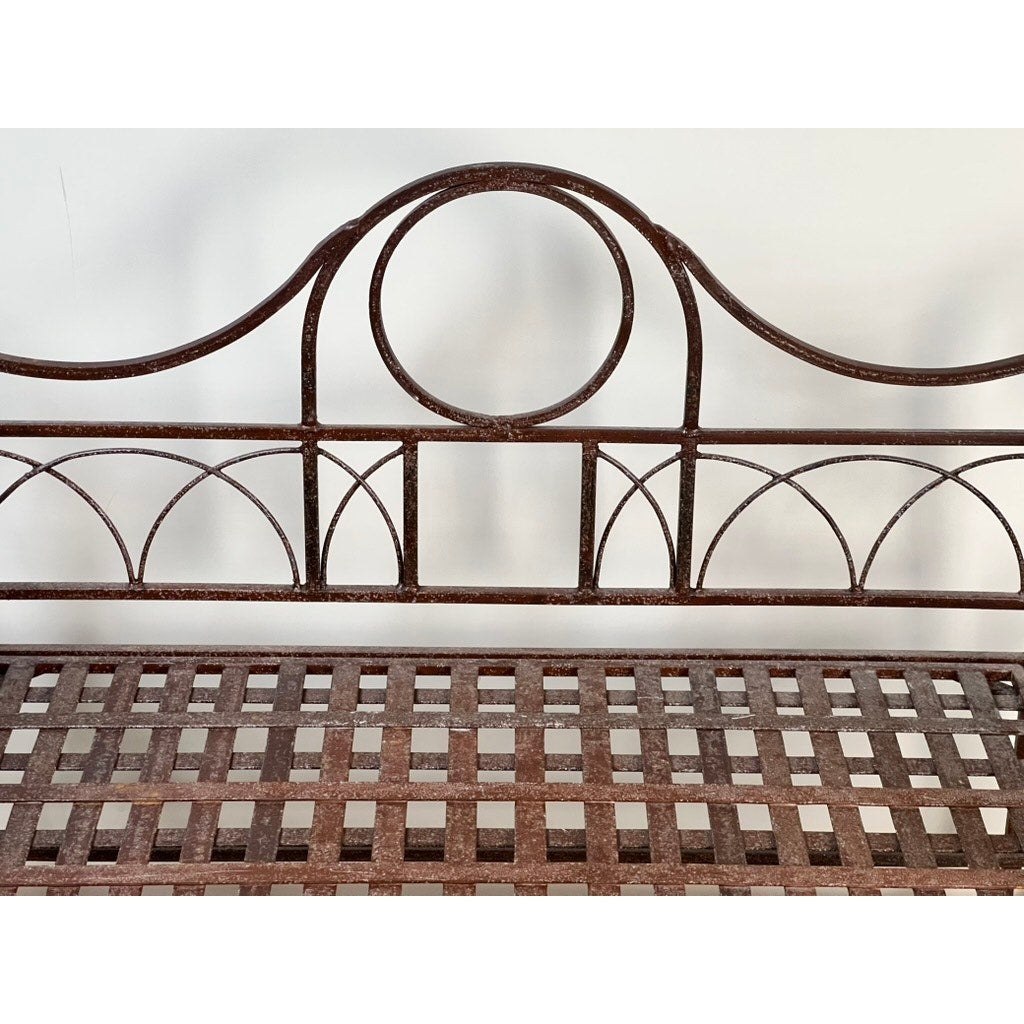 Vintage Regency Style Wrought Iron Porch Glider with a lattice seat and decorative circular and arch-shaped backrest, evoking a vintage garden look, shown against a plain white wall. Brand: None/Unknown.