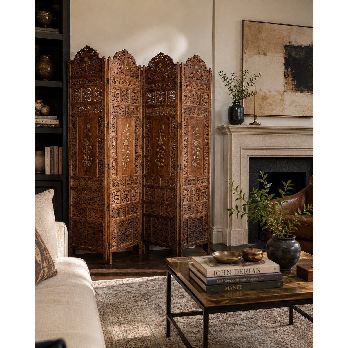A Pearl City Antiques Early 20th Century Anglo-Indian Carved Teak Four-Panel Screen with Applied Brass Floral Decoration stands by a fireplace in a cozy living room, complemented by a beige sofa, books, potted plants, and neutral-toned decor.
