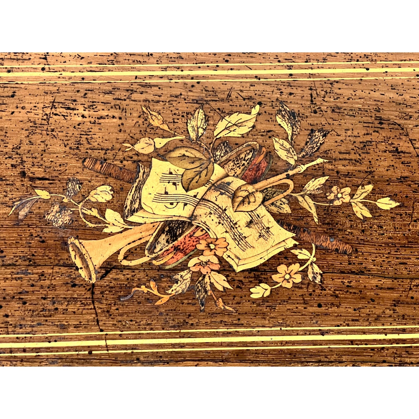 The Antique Swiss 12 Tune Music Box c. Late 19th Century features detailed wood marquetry with a trumpet, French horn, sheet music, and floral motifs on a brown speckled background with decorative lines, evoking Victorian era elegance.