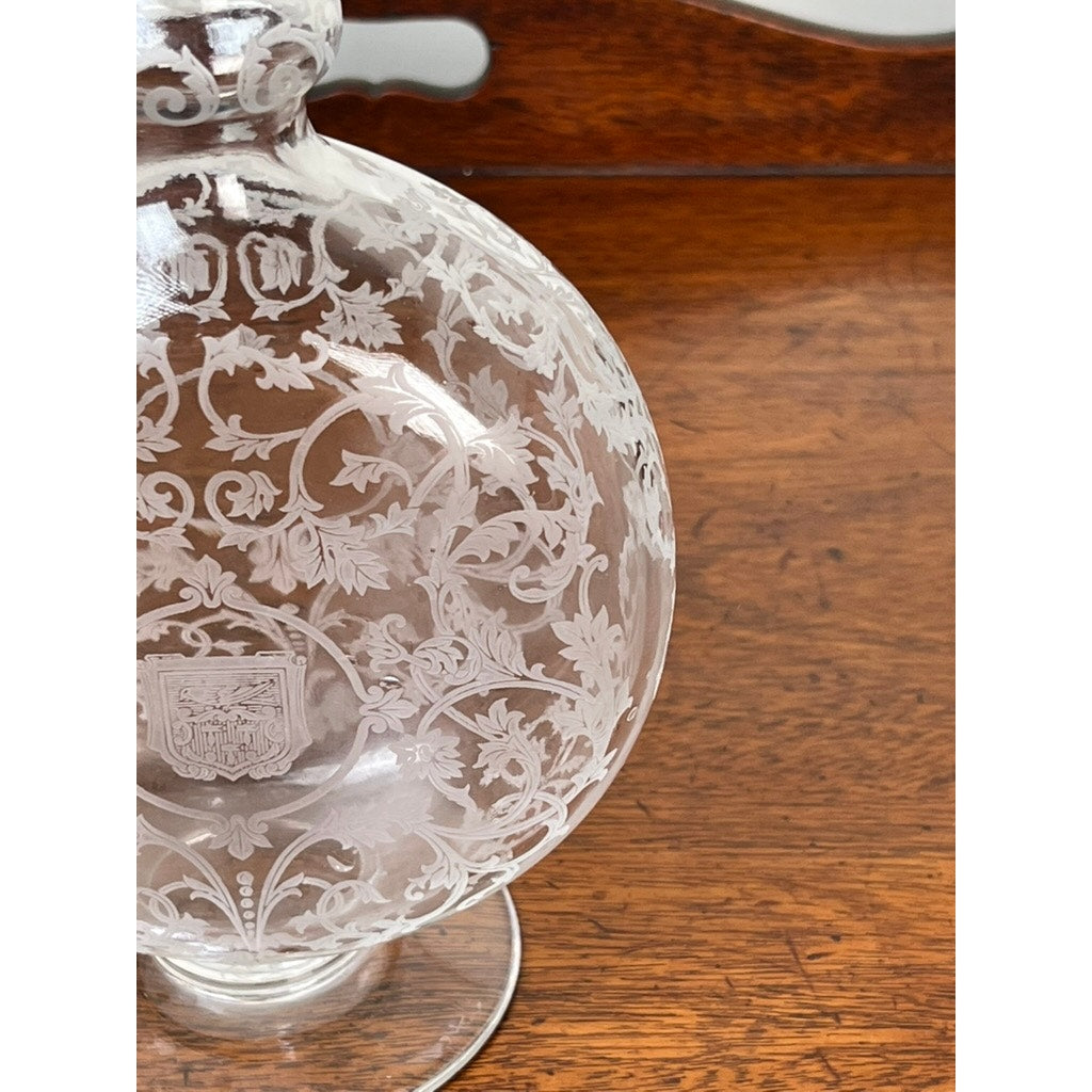 Close-up of a Vintage Baccarat Crystal Decanter in the "Michelangelo" pattern for Martell Cognac c. 1930, featuring intricate etchings and a small crest, set on a polished wooden surface.