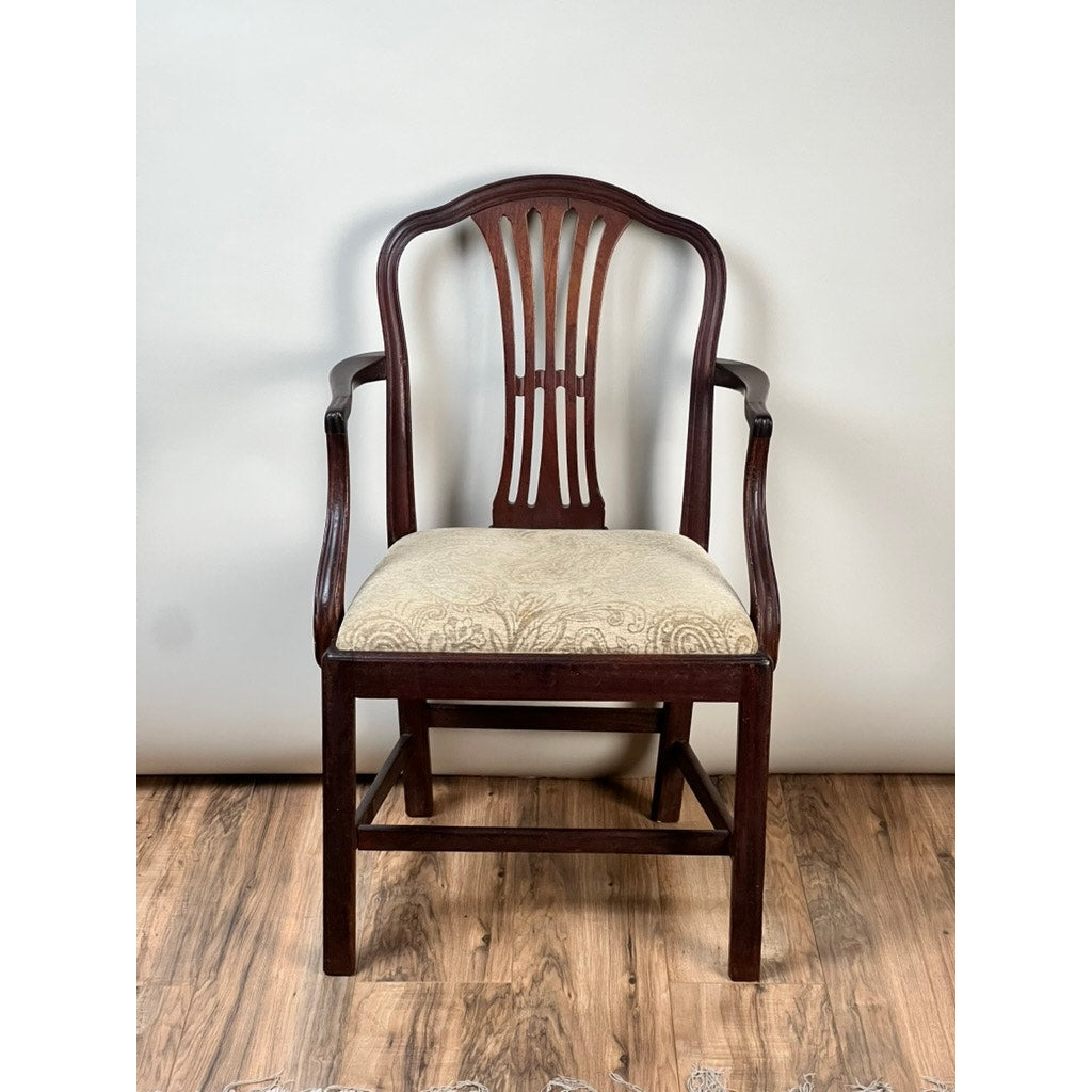 An Antique English George III Mahogany Hepplewhite Armchair from the early 19th century features a decorative curved back with vertical slats and a beige patterned upholstered seat, displayed on a wooden floor with a plain light background.