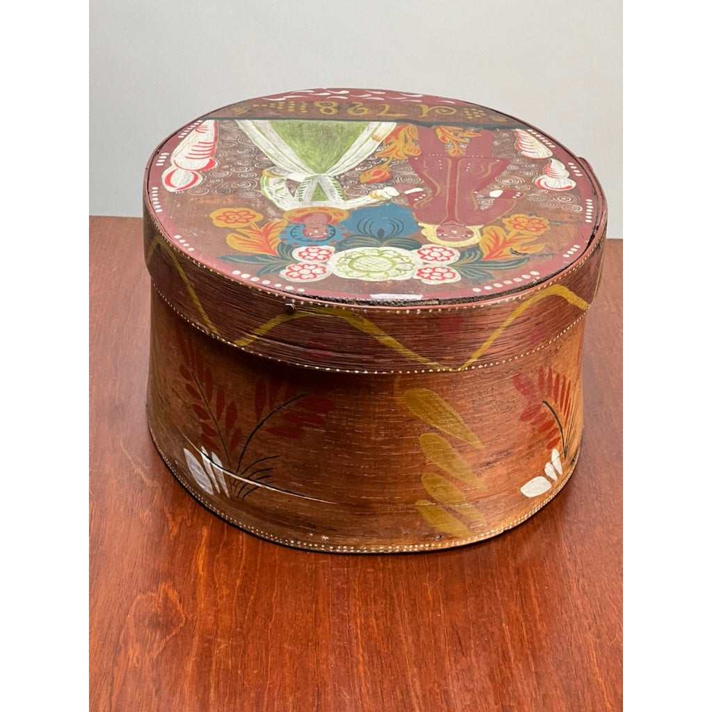 Antique Swedish Polychrome Painted Marriage Box dated 1798. This round bentwood box features colorful Scandinavian folk art with floral motifs and figures, ornamented sides, and rests on a reddish-brown wooden surface.