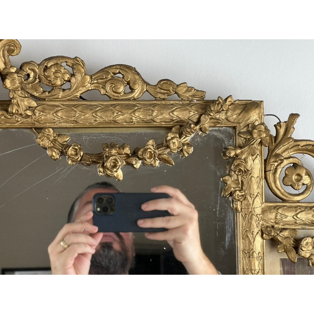 A person snaps a photo with their phone, partially visible in the reflection of an Exceptional Antique Louis XV Style Three Panel Mirror flanked by images of Napoleon, featuring ornate gold floral designs.