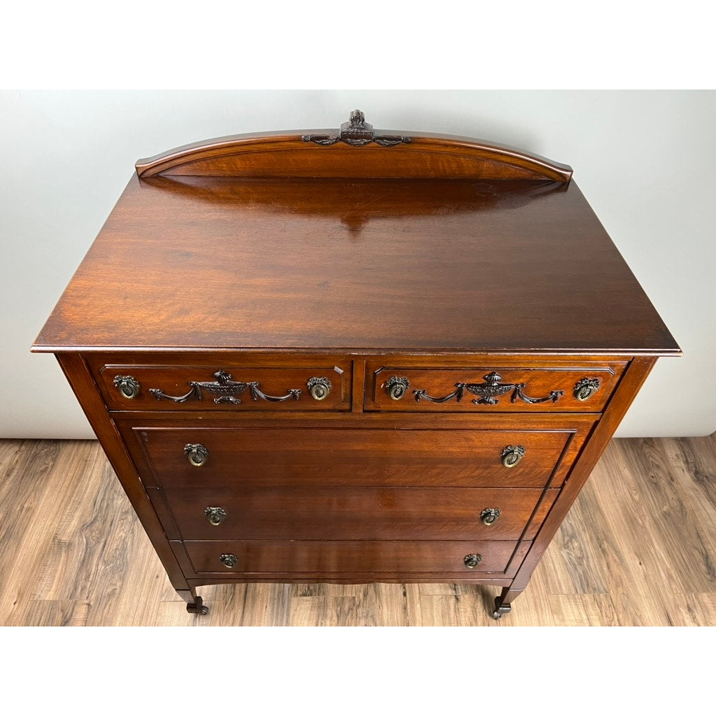 An Antique Depression Era Mahogany Two Over Three Chest of Drawers, c. 1930s, features ornate metal handles, decorative carvings, short legs, and a curved back panel—an elegant vintage piece for showcasing on hardwood flooring. Brand: None/Unknown.