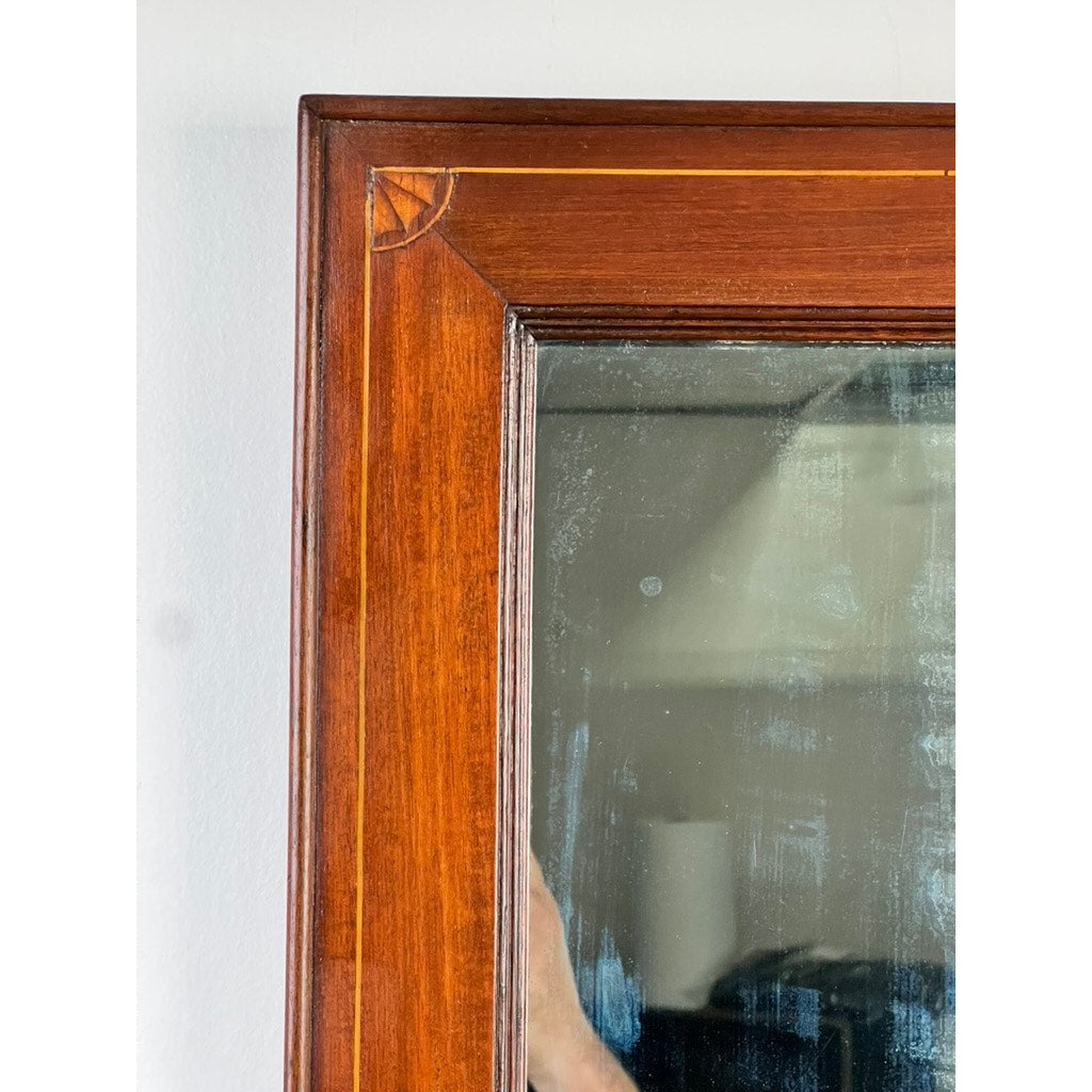 Close-up of the top left corner of an American Federal Mahogany Wall Mirror with fan inlay and original hand silvered glass, circa 1810–1825. The mirror’s surface reflects a blurred interior scene and part of a person’s arm.