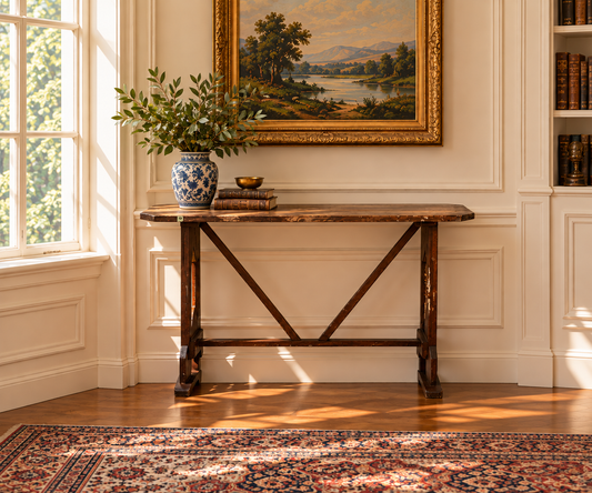 An Antique Rustic Italian Fratino Trestle Table c. Late 19th Century set against a paneled wall, topped with a blue and white vase holding greenery and a stack of books.