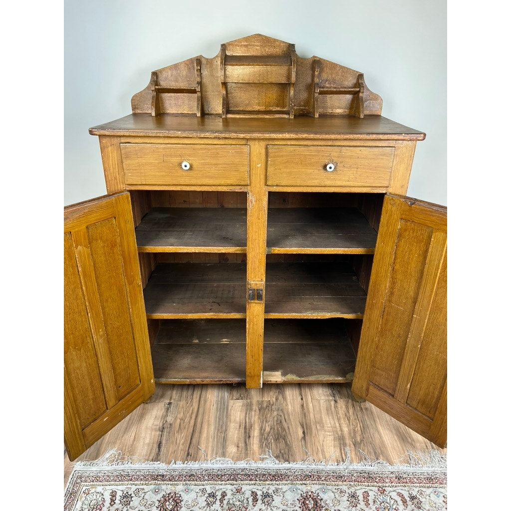 The Antique Victorian Country Grain Painted Jelly Cupboard c. 1870 features two open drawers, lower doors with shelves, and a decorative hutch. It stands on a wooden floor with part of a patterned rug visible in front. Brand: Unknown.