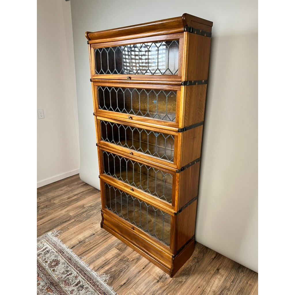 A Vintage Globe Wernicke Leaded Glass Five Stack Barrister Bookcase by Globe Wernicke stands against a light wall on a wooden floor, next to a patterned rug.