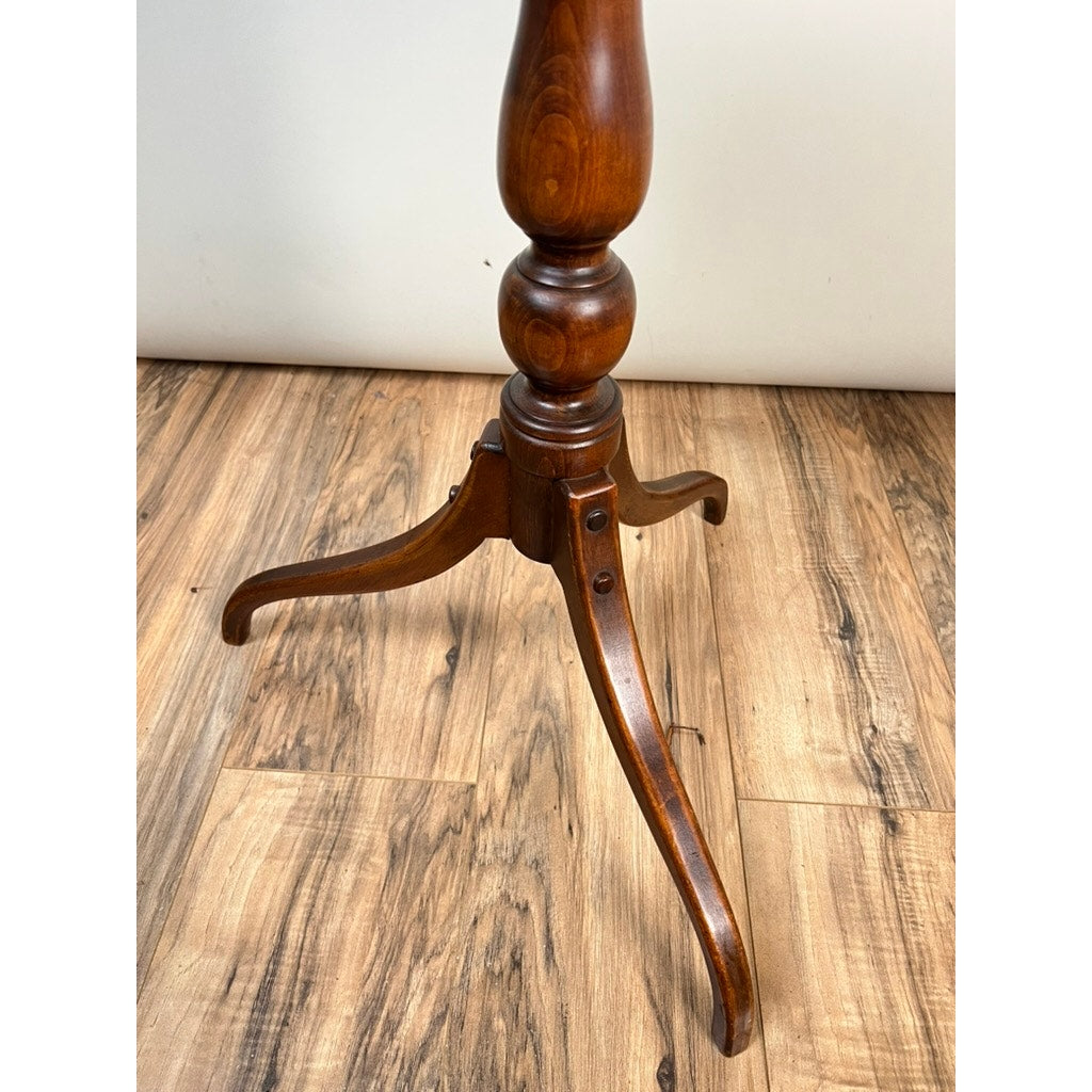 A close-up of the Stickley Vintage Federal Style Cherry Octagonal Tilt Top Candlestand shows its carved wooden pedestal leg with three curved feet on a hardwood floor, highlighting the rich cherry finish and Federal-inspired details.