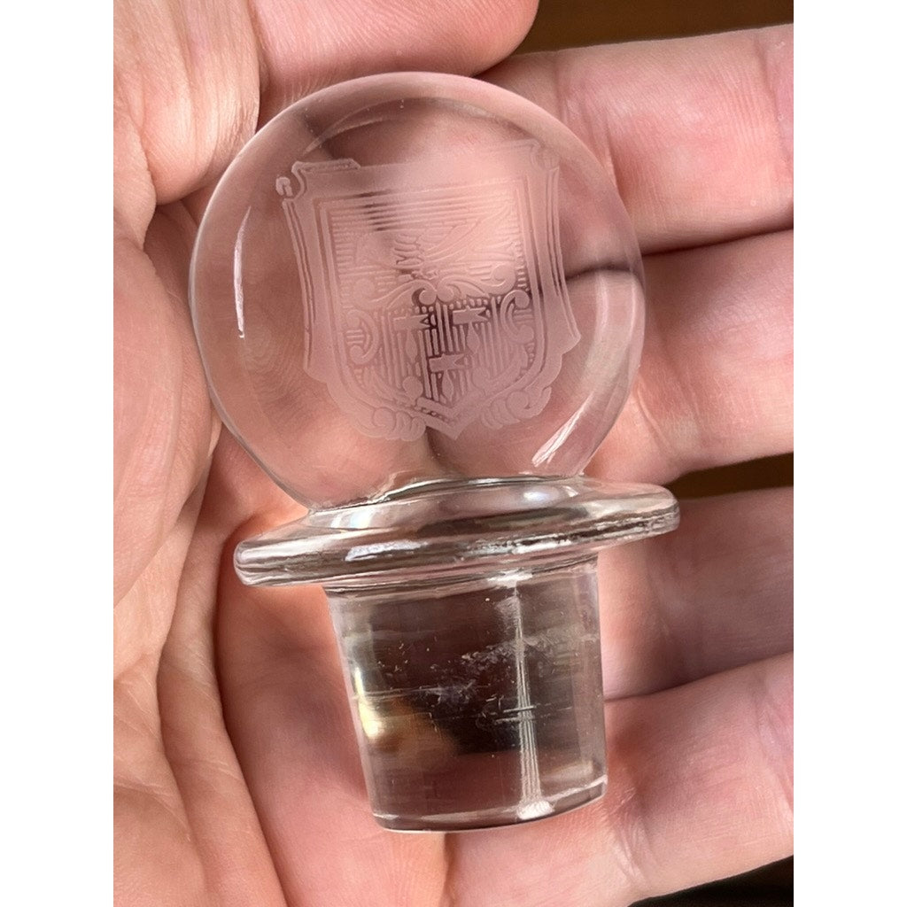 A hand holds a Baccarat crystal decanter stopper from the vintage "Michelangelo" pattern, made for Martell Cognac circa 1930, featuring a round top and engraved shield—an elegant detail of classic Baccarat design.