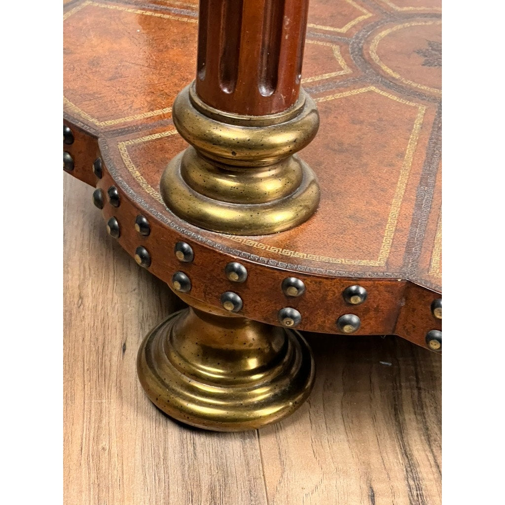 Close-up of a Maitland Smith Vintage Leather-Clad Occasional Table leg featuring brass nailhead trim, gold metallic accents, and intricate inlay detail, shown on a hardwood floor.