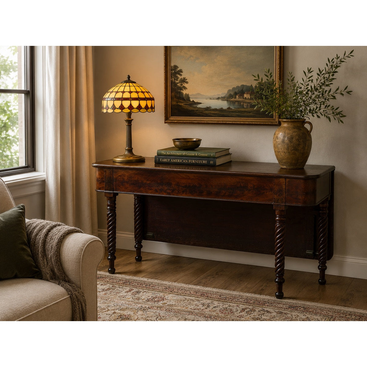 An American Classical Mahogany Single Drop-Leaf Table with Spiral-Twist Legs, c. 1830–1845 from Pearl City Antiques displays a stained-glass lamp, books, a bowl, and a large rustic vase with green branches. Nearby, a window framed by beige curtains and a sofa are visible.