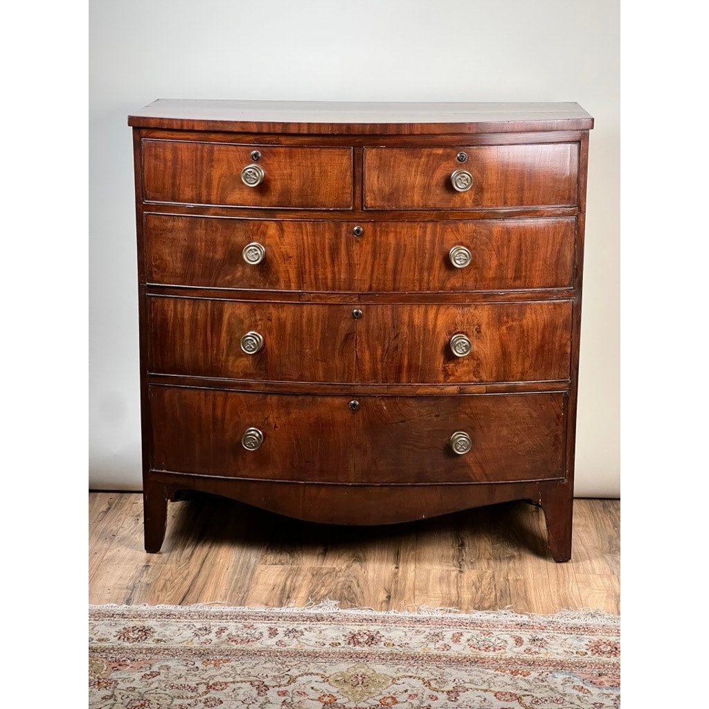 The Antique George III Mahogany Bowfront Chest on French Feet, c. late 18th century, features four large and two small drawers with round metal handles, a polished finish, and stands on short legs atop a wooden floor.