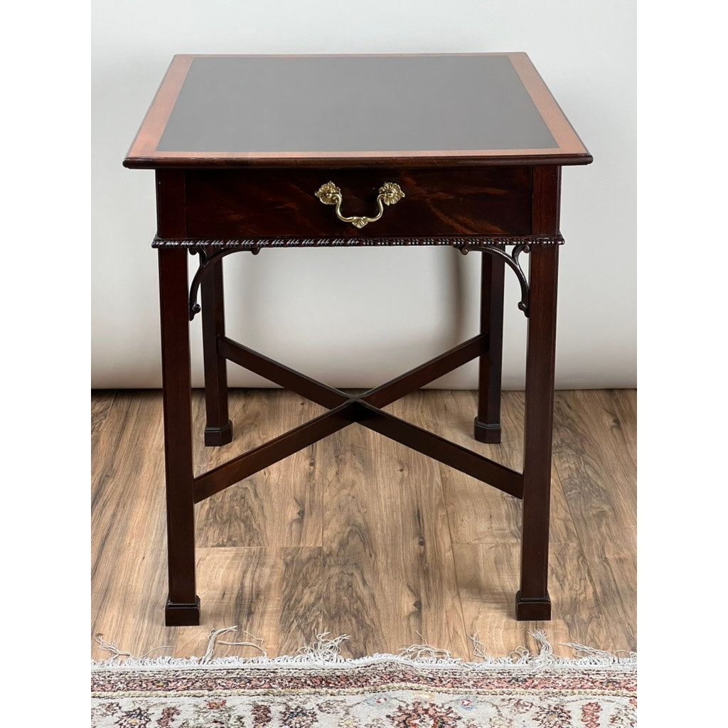 The Stickley Vintage Federal Style X Stretcher One Drawer End Table features a dark polished finish, ornate brass handle, and X-shaped stretcher, shown on a wooden floor beside a patterned rug.