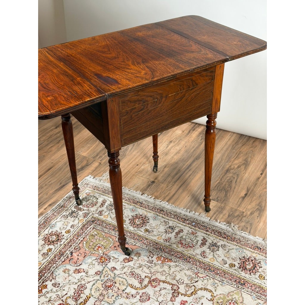 English Regency Rosewood Two-Drawer Drop-Leaf Work Table with Brass and Satinwood Inlay, circa 1820–1840, featuring slender turned legs and brass casters, showcasing fine 19th-century craftsmanship.