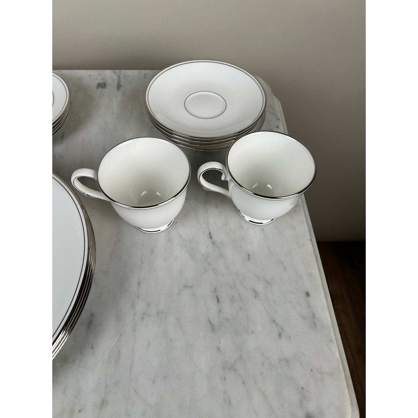 Two Lenox Federal Platinum Fine English Bone China teacups with silver rims rest on marble, beside three matching saucers and part of a large plate—elegant vintage tableware from the Lenox service for four.