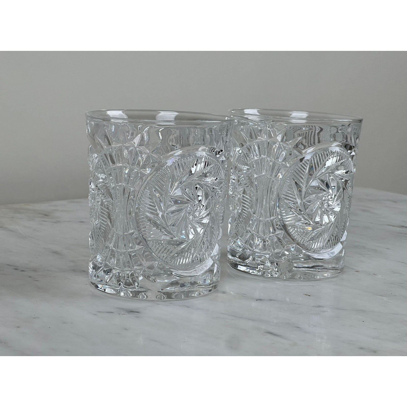 A pair of Fostoria Stowe Double Old Fashioned Tumbler Glasses are displayed on white marble with a plain light gray background.