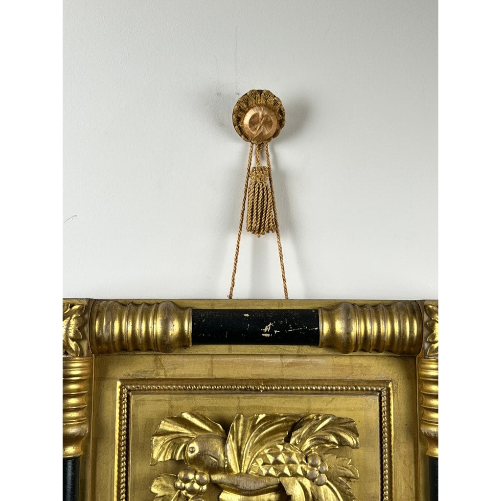 An Antique Federal Period Giltwood Mirror with rosette corners and cornucopia c. 1830 hangs from a gold cord on an ornate round gold wall hook with a tassel, featuring carved floral and leaf details. Brand: Unknown.