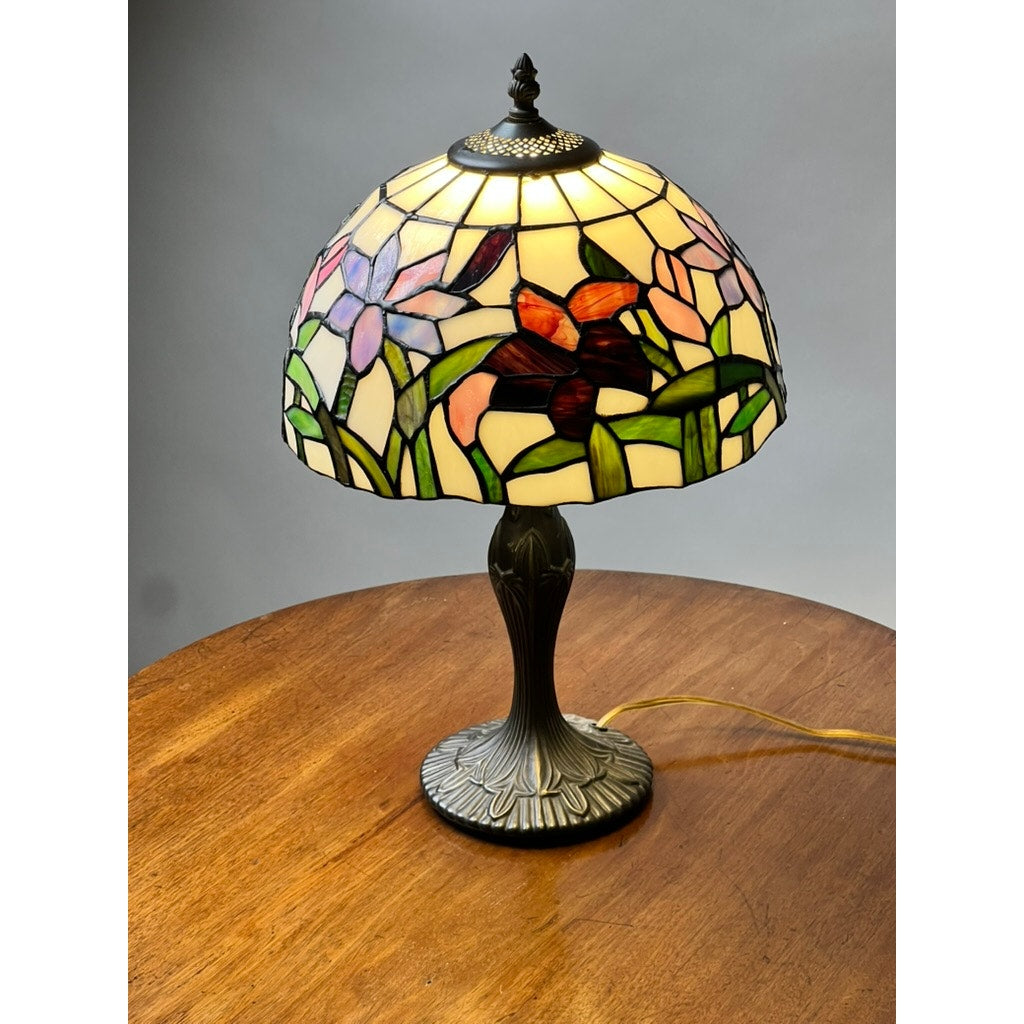 The Vintage Tiffany Style Floral Stained Glass Table Lamp features a stained glass shade with purple and red flowers atop an ornate metallic base, adding elegance to any room. Brand: Unknown.