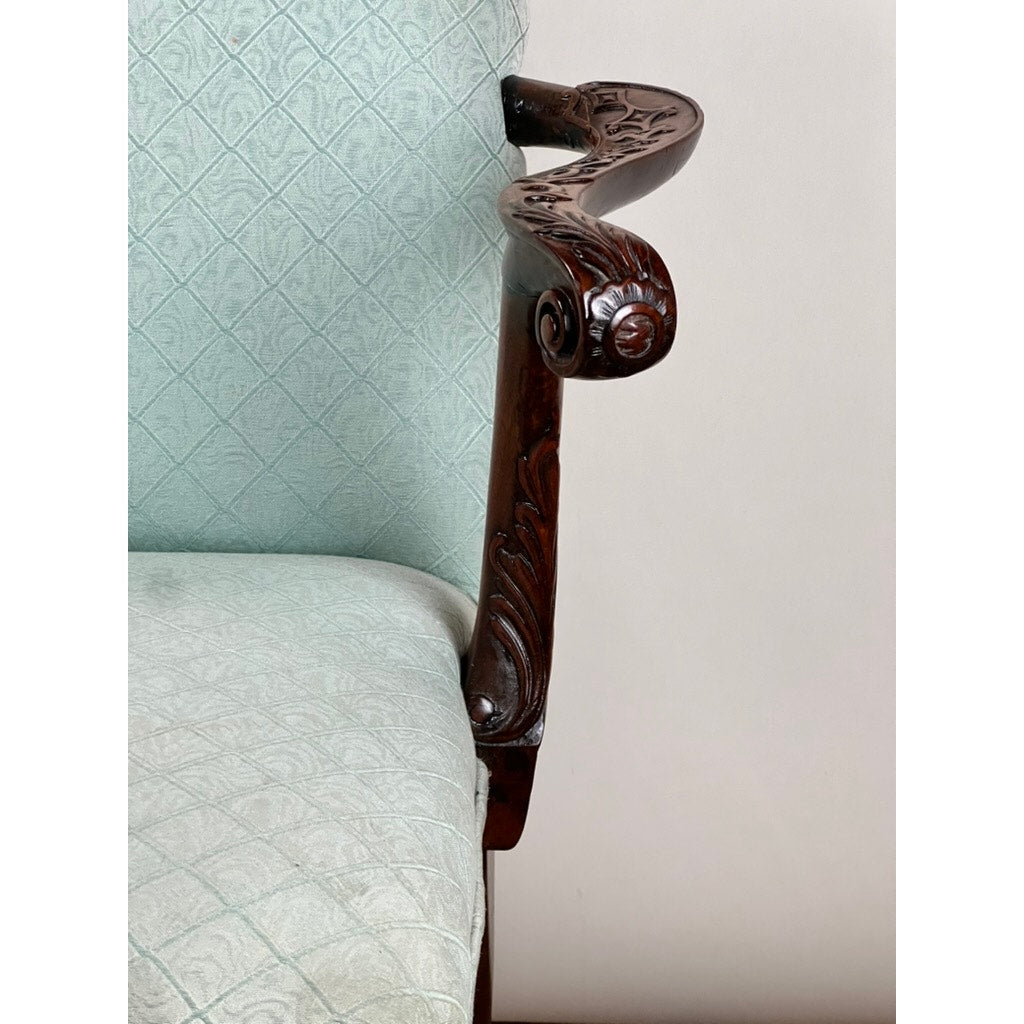 Close-up of the ornate mahogany armrest of an Antique George II Mahogany Gainsborough Open Arm Chair c. Mid 19th Century, featuring light blue diamond-pattern upholstery, set against a plain white background.
