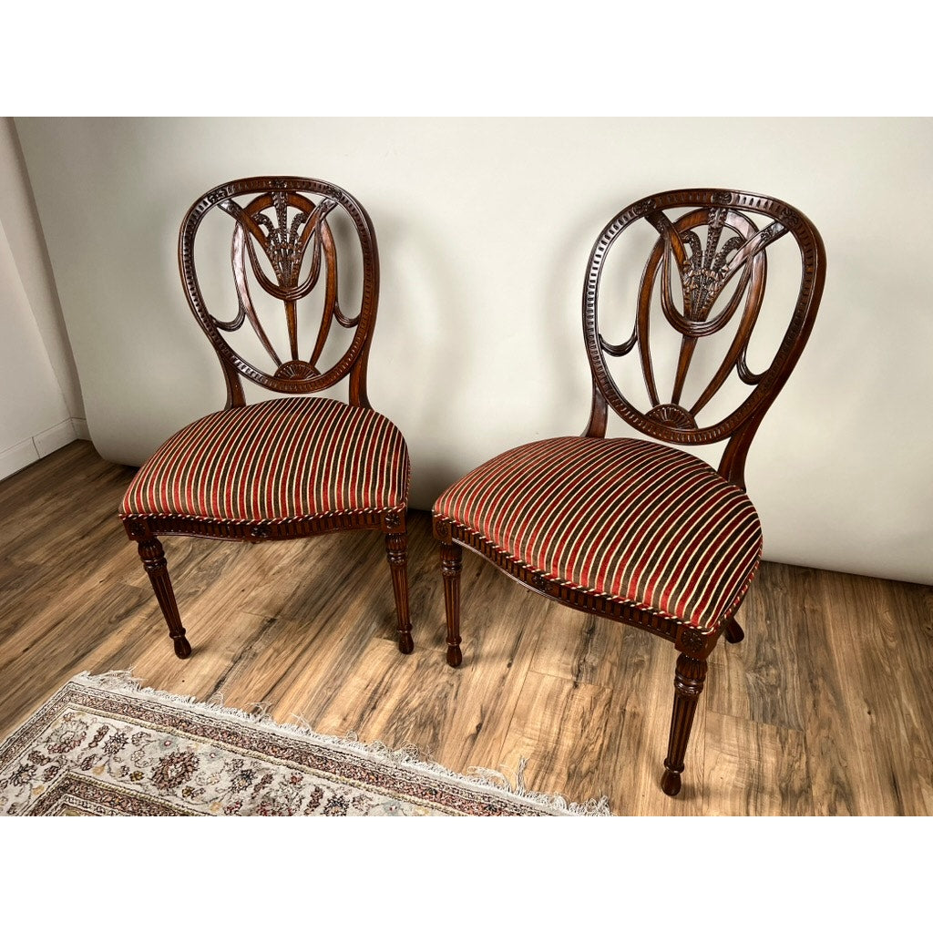 A Vintage Pair Wheel Back Side Chairs by Ardley Hall features ornate carved backs and red-striped seats, showcasing classical English design on a wooden floor beside a patterned rug and plain white wall.