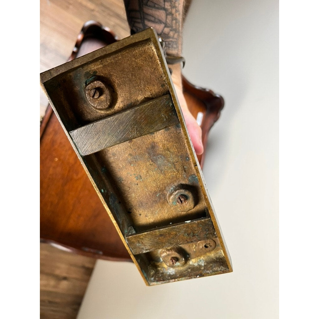 A close-up shows a hand holding the Jean-Baptiste Clesinger “Taureau Romain” bronze sculpture (Barbedienne Foundry, Rome 1858) with screws and rectangular sections, viewed from beneath; a wooden chair and hardwood floor appear in the background.