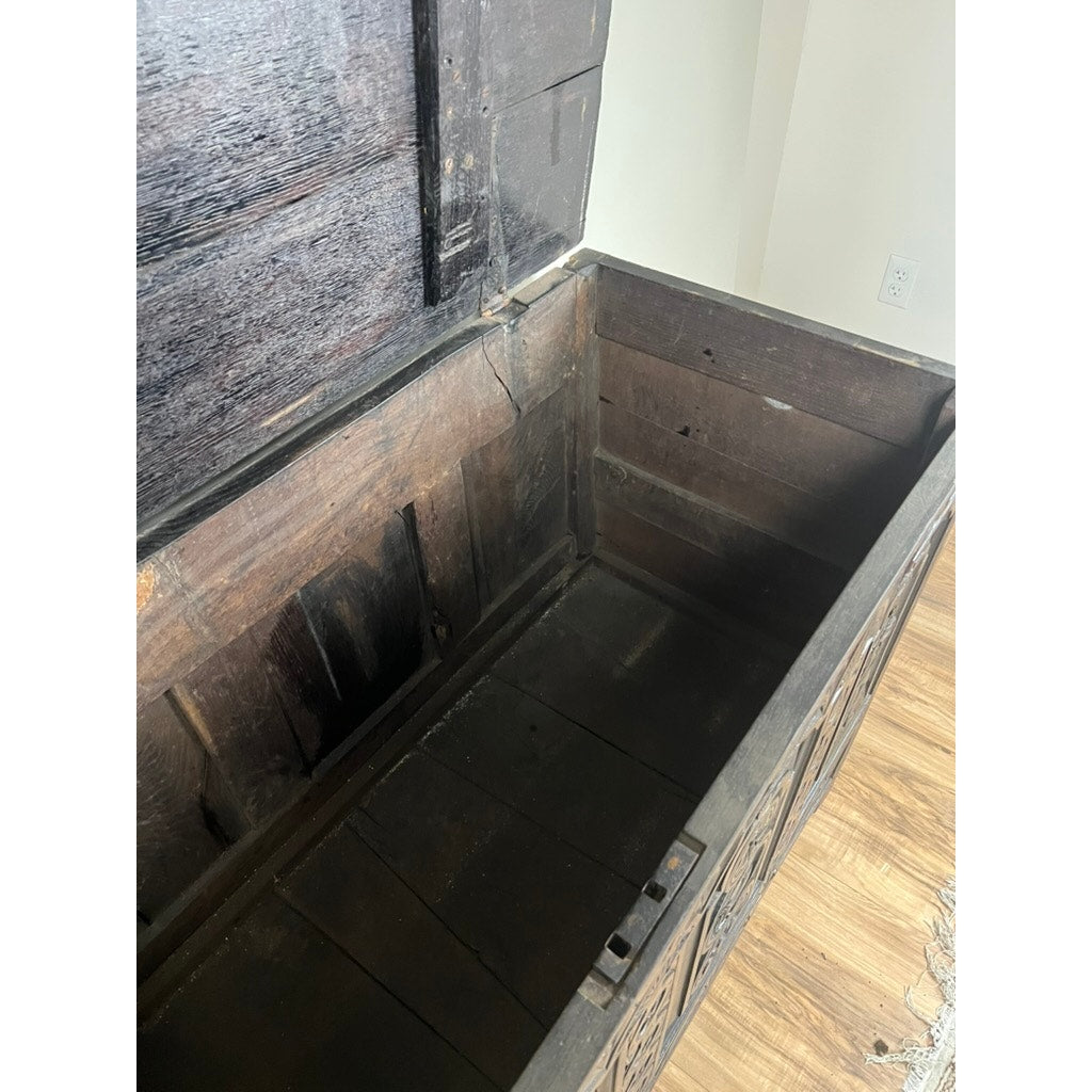 An Antique 18th Century Charles II Style Mule Chest—possibly Irish or Scottish—rests on a wooden floor near a light wall and outlet, its ornate carvings and dark interior suggesting secret drawers and hidden treasures. Brand: Unknown.