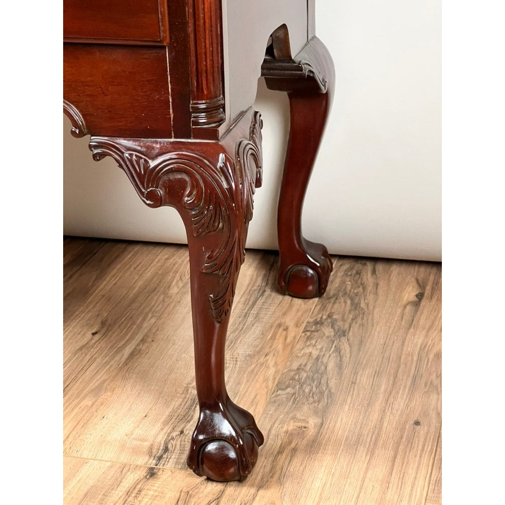 Close-up of a claw-and-ball foot leg on the Vintage Solid Mahogany Chippendale Style Lowboy by Councill Craftsmen, showcasing ornate carved details and polished antique elegance against a wood floor.